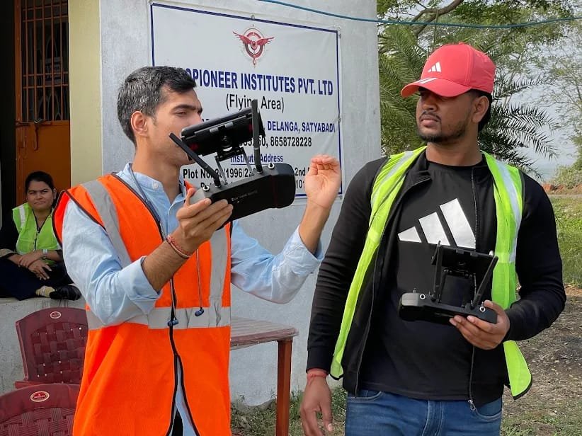 Instructor and trainee with remote controllers in front of the Aeropioneer Institutes flying area signboard