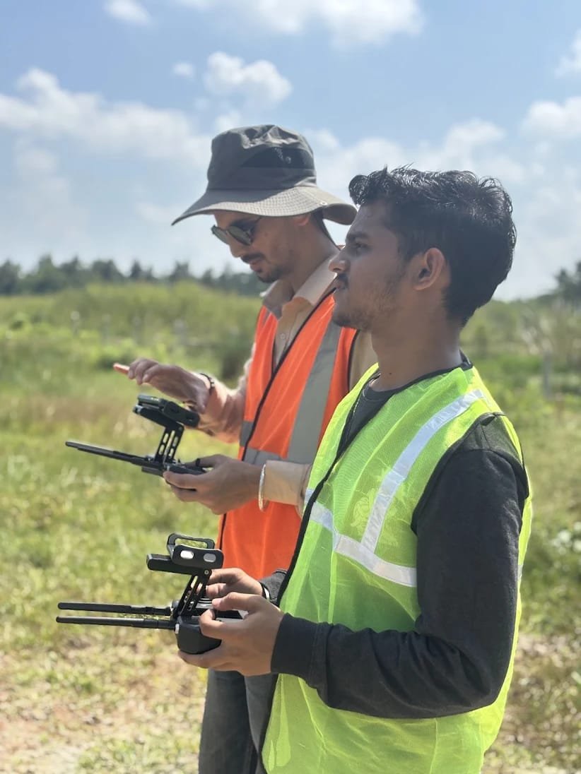Two remote pilots operating drone controllers outdoors under an open sky